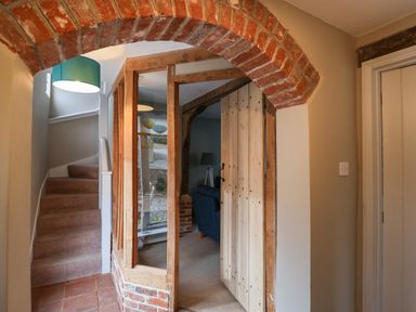 A hallway with a brick arch, wooden door, glass panels, staircase with carpet, and a blue lamp shade at 1 The Old Coach House Huntingfield Near Laxfield