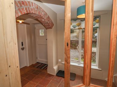 An entryway with a brick archway a white door a striped rug tile flooring and a window with a teal lamp at 1 The Old Coach House Huntingfield Near Laxfield
