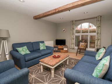 A living room with blue sofas green cushions a wooden coffee table a patterned rug and a TV on a wooden stand at 1 The Old Coach House Huntingfield Near Laxfield