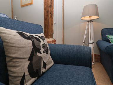 A living area with blue fabric armchairs a cushion with a cow design a floor lamp and exposed wooden beam at 1 The Old Coach House Huntingfield Near Laxfield
