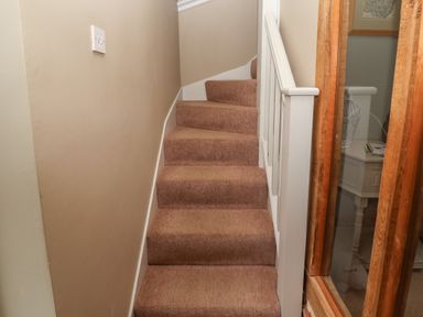 A carpeted staircase with white wooden railing next to a glass window and beige walls at 1 The Old Coach House Huntingfield Near Laxfield