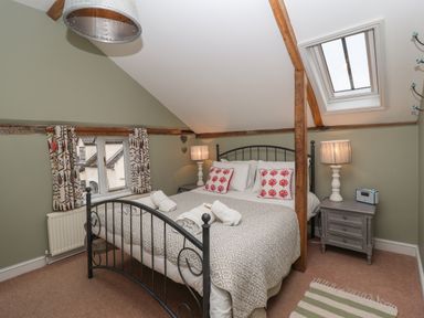 A bedroom with a double bed and bedside tables under a slanted ceiling with wooden beams at 1 The Old Coach House Huntingfield Near Laxfield