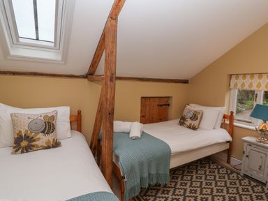 A bedroom with two single beds a window with a patterned blind and a bedside table with a lamp at 1 The Old Coach House Huntingfield Near Laxfield