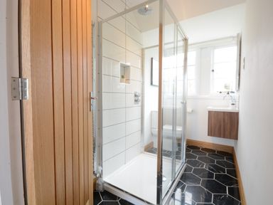 A bathroom with a glass shower enclosure wooden door black hexagonal floor tiles and a wooden vanity at Ash Tree Cottage Aldringham