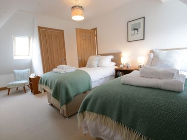 A bedroom with two single beds covered with green throws and white towels by a window and two wooden doors at Ash Tree Cottage Aldringham