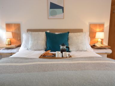 A bed with pillows and breakfast tray with coffee and croissants between two bedside tables with lamps at Ash Tree Cottage Aldringham