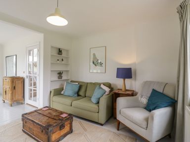 A living room with a green sofa and gray armchair with cushions a wooden chest coffee table and a lamp on a side table at Ash Tree Cottage Aldringham