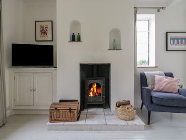 A living room with a lit wood stove fireplace baskets and a blue armchair at Ash Tree Cottage Aldringham