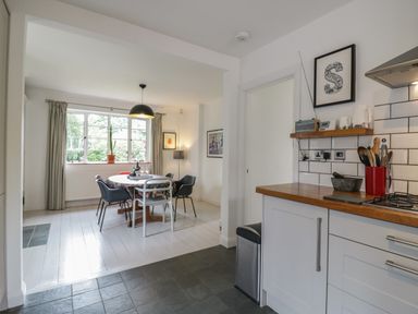 A kitchen area with a wooden countertop and a dining area with a round table and chairs by a window at Ash Tree Cottage Aldringham