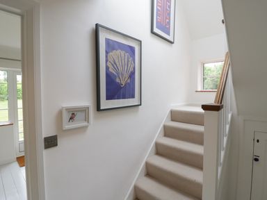 A carpeted staircase with white walls and framed artwork on the wall at Ash Tree Cottage Aldringham