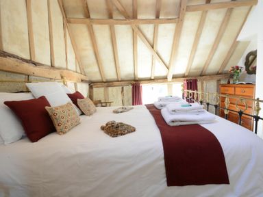 A bedroom with a bed made with white sheets and red runners near a wooden dresser and a window at Yew Tree Farm Barn Worlingworth