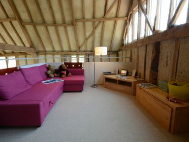 A loft room with a pink sofa two stuffed animals a floor lamp and wooden cabinets at Yew Tree Farm Barn Worlingworth near Framlingham