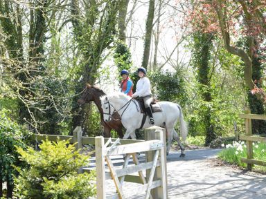 Two people riding horses on a path surrounded by trees and greenery at Yew Tree Farm Barn Worlingworth near Framlingham