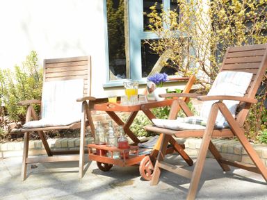 Two wooden chairs with cushions and a wooden tray table holding drinks and flowers outside a house at Yew Tree Farm Barn Worlingworth