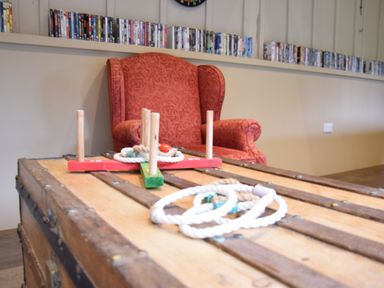 A wooden table with a ring toss game and a red armchair with a shelf of DVDs behind it at Yew Tree Farm Barn Worlingworth