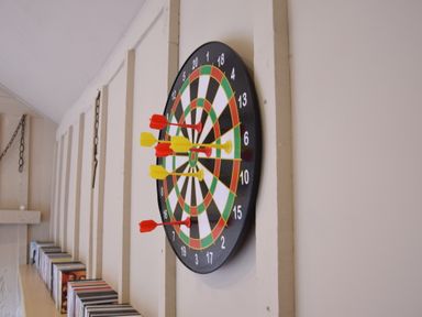A dartboard with red and yellow darts on a wall above shelves with CDs at Yew Tree Farm Barn Worlingworth