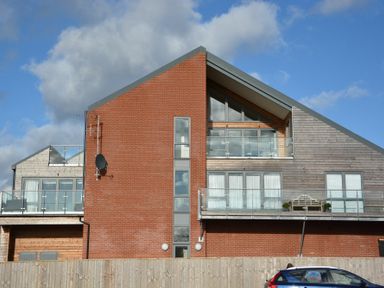A modern building with brick and wood exterior and glass balconies with a blue car in front at King George Penthouse in Aldeburgh