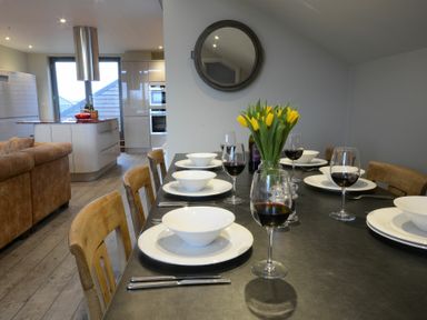 A dining table set with white bowls plates wine glasses and yellow flowers in a kitchen area at King George Penthouse in Aldeburgh