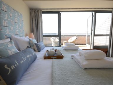 A bedroom with a bed with decorative pillows and folded towels facing a balcony with wicker chairs at King George Penthouse in Aldeburgh