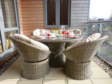 A balcony with a round glass table and six wicker chairs with cushions at King George Penthouse in Aldeburgh