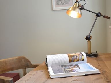 A wooden desk with an open book and a brass desk lamp in a room at King George Penthouse in Aldeburgh