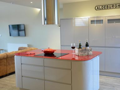 A kitchen with a red countertop island with a pot wine bottles and a glass in Aldeburgh Penthouse in Aldeburgh