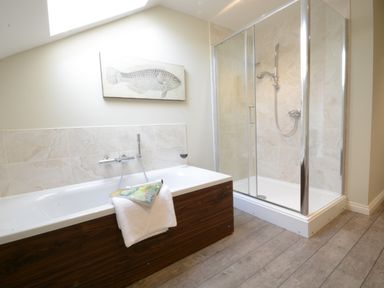 A bathroom with a bathtub and a glass shower enclosure with tiled walls at King George Penthouse in Aldeburgh