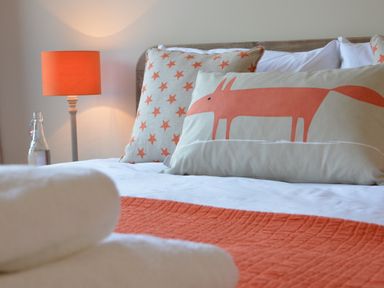 A bed with decorated pillows an orange throw a lamp and a bottle of water at King George Penthouse in Aldeburgh