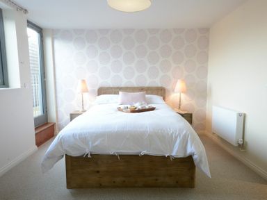 A bedroom with a wooden bed white bedding two bedside tables with lamps and a window at King George Penthouse in Aldeburgh