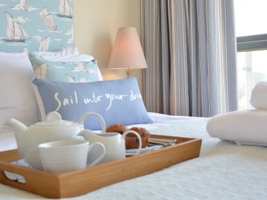 A bedroom with a bed with pillows including one with sailboat prints and a tray with tea set and muffins at King George Penthouse in Aldeburgh