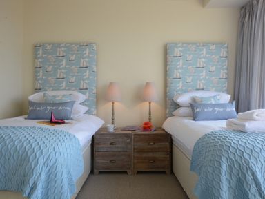 A bedroom with two single beds with blue patterned headboards a wooden bedside table with two lamps and folded towels at King George Penthouse in Aldeburgh