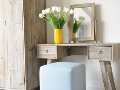 A wooden dressing table with a mirror and a yellow vase with white flowers and a light blue stool at King George Penthouse in Aldeburgh