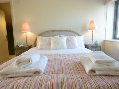 A bedroom with a bed with pillows and folded towels on a striped bedspread and two bedside tables with lamps