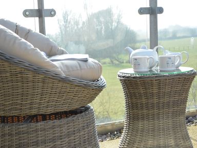 A wicker chair with cushions and a wicker table with a teapot and two cups on a balcony at King George Penthouse in Aldeburgh