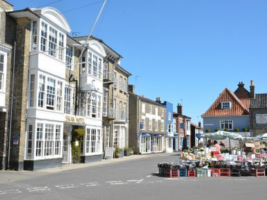 A street with a white building labeled Swan Hotel and market stalls with various goods on the right in Blythburgh near Southwold