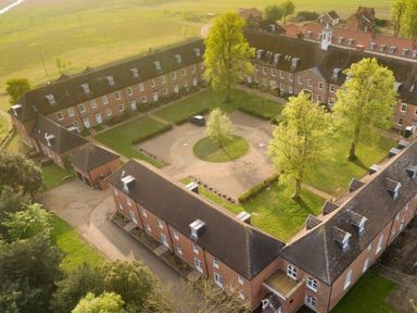 An aerial view of a brick building complex surrounding a courtyard with trees and a circular driveway at Saffron Blythview in Blythburgh near Southwold