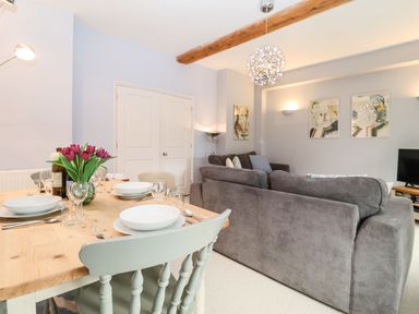 A dining table set with plates glasses and a vase of flowers next to gray sofas and wall art at Saffron Blythview in Blythburgh near Southwold
