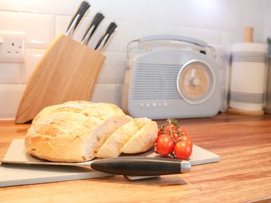A kitchen counter with sliced bread cherry tomatoes knife a knife block radio and paper towels