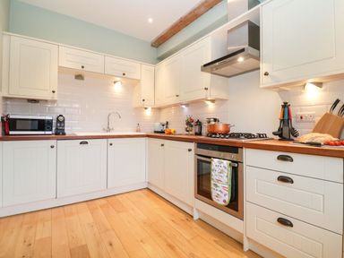A kitchen with wooden floor white cabinets a microwave a coffee machine a stove with a pot and cooking utensils at Saffron Blythview in Blythburgh near Southwold