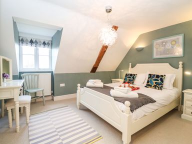 A bedroom with a white bed and bedside tables a chair by the window and a desk with a mirror at Saffron Blythview in Blythburgh near Southwold