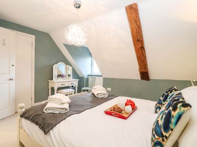 A bedroom with a bed with pillows and a tray with tea set and pastries a dressing table and chair under a sloped ceiling with wooden beam at Saffron Blythview in Blythburgh near Southwold