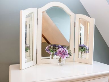 A white dressing table with a three-panel mirror and a glass vase with purple flowers at Saffron Blythview in Blythburgh near Southwold
