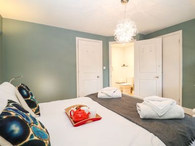 A bedroom with a bed with towels and a tea tray with a teapot and cups near two closed doors and one open door showing a bathroom at Saffron Blythview in Blythburgh near Southwold