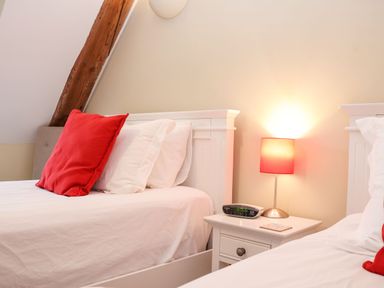 A bedroom with two white beds and red pillows with a bedside table holding a lamp and a digital clock at Saffron Blythview in Blythburgh near Southwold