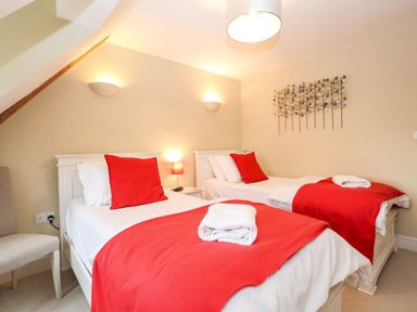 A bedroom with two single beds with red blankets and pillows a chair and wall decorations at Saffron Blythview Blythburgh near Southwold