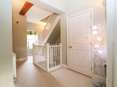 A stairway with white railing and a door next to a decorative light in a hallway at Saffron Blythview in Blythburgh near Southwold