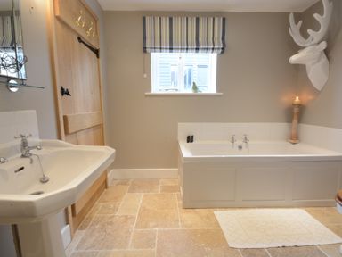 A bathroom with a bathtub a sink a wooden door and a window with striped blinds at Bird Cottage Burgh Near Grundisburgh