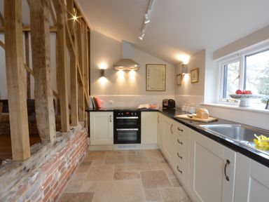 A kitchen with white cabinets black countertops a stainless steel oven and extractor fan next to a window at Bird Cottage Burgh Near Grundisburgh