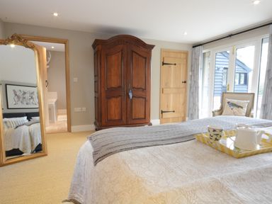 A bedroom with a large wooden wardrobe a full length ornate mirror with a gold frame a bed with a tea tray and teapot and cups a chair with a bird cushion and glass doors leading outside at Bird Cottage Burgh Near Grundisburgh