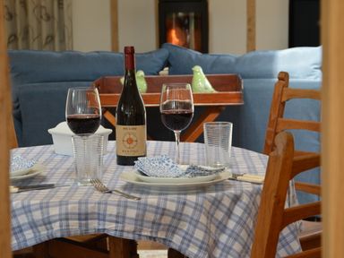 A dining table set with wine glasses plates and blue checkered tablecloth in a living room with blue sofas at Bird Cottage Burgh Near Grundisburgh